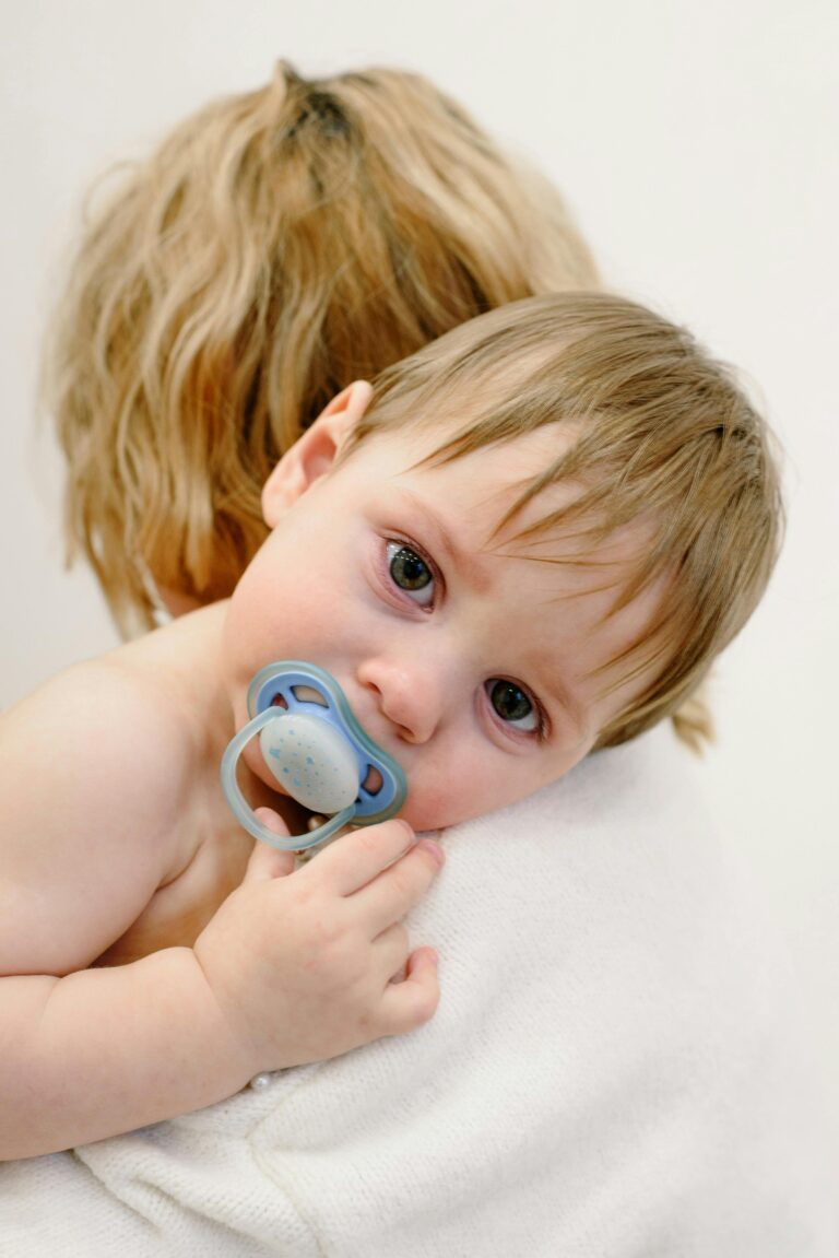 A baby with pacifier rests on mother's shoulder, showing affection and comfort.